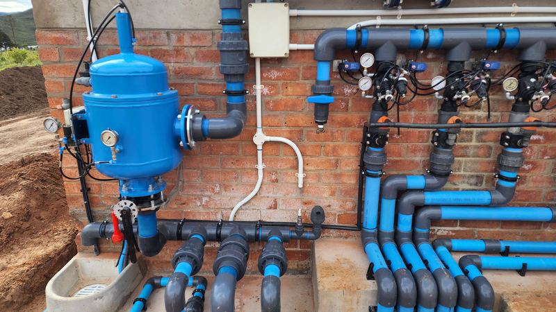 Blue irrigation manifold pipework on a brick wall