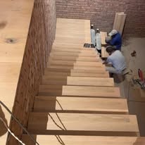 Two people installing timber stair treads against a brick wall